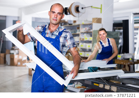 Worker in workwear is standing with window frame from pvc profile 37871221