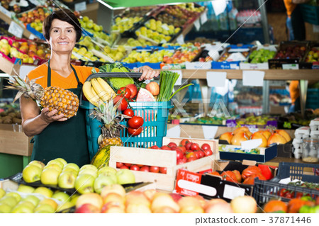 Smiling female seller is standing with basket with fruits 37871446