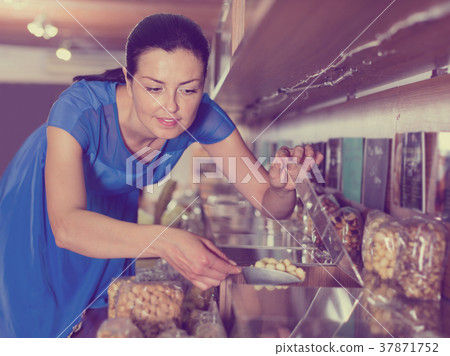 Woman taking nut by weight with scoop in organic shop 37871752