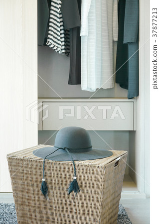 Black hat on basket with cloths hanging in closet Black hat on basket with cloths hanging in closet 37877213