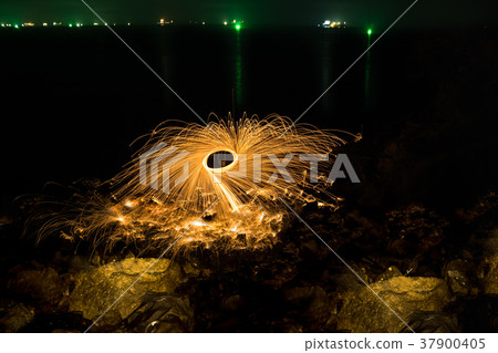Man showing spinning fire on rocky beach at night 37900405