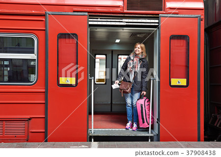 Woman tourist with suitcase coming out of train at station 37908438