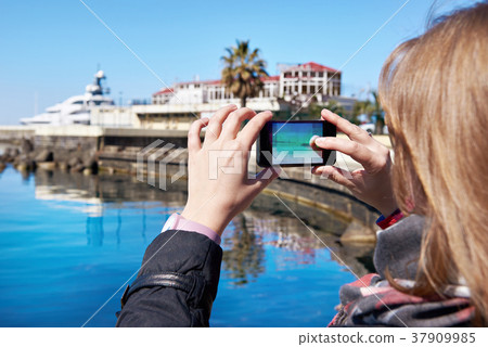 Girl photographs on mobile phone seashore and pier Girl photographs on mobile phone seashore and pier 37909985