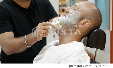 Barber is shaving his client in old fashion manner Barber is shaving his client in old fashion manner 37913609