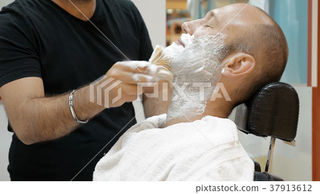 Barber is shaving his client in old fashion manner Barber is shaving his client in old fashion manner 37913612