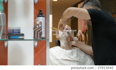 Barber is shaving his client in old fashion manner 37913640