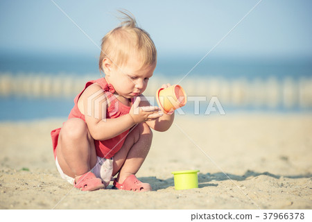Baby girl in red dress playing on sandy beach near 37966378