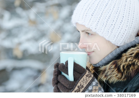 Girl in winter clothes drinking tea from a mug 38017169