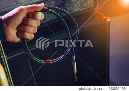 The bass guitarist connects the bass guitar to the amplifier on the stage. 38020493