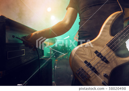 The bass guitarist connects the bass guitar to the amplifier on the stage. 38020498