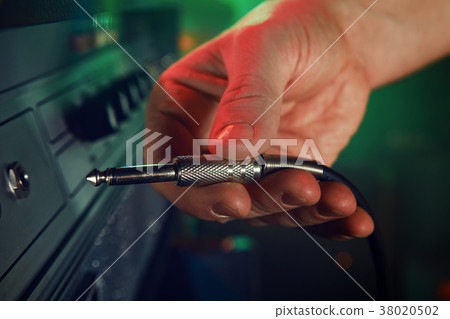 The bass guitarist connects the bass guitar to the amplifier on the stage. 38020502