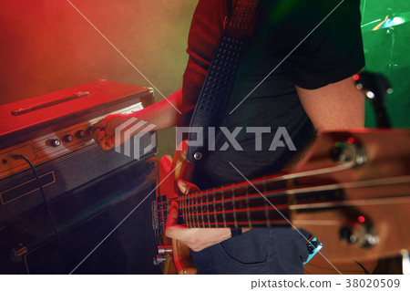 The bass guitarist connects the bass guitar to the amplifier on the stage. 38020509