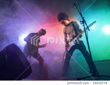 Rock band performs on stage. Guitarist, bass guitar and drums. 38020534