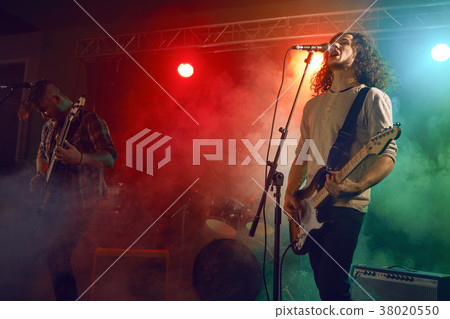 Rock band performs on stage. Guitarist, bass guitar and drums. 38020550