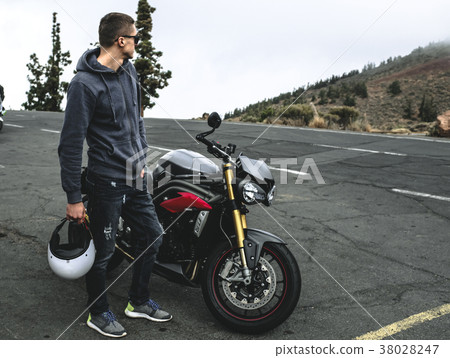 rider stand on a mountain next to motorcycle rider stand on a mountain next to motorcycle 38028247