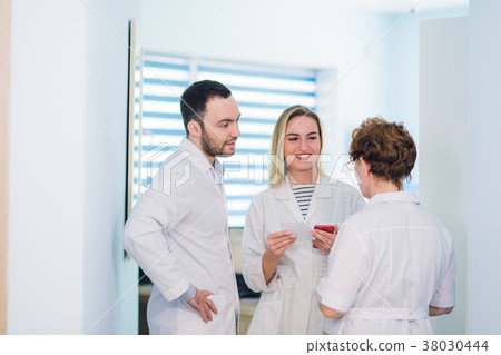 Mature doctor discussing with nurses in a hallway Mature doctor discussing with nurses in a hallway 38030444