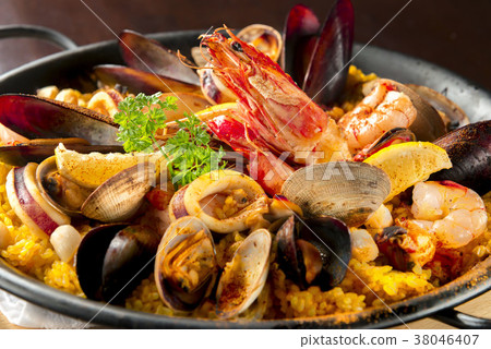 一份海鮮飯，上面鋪滿了蝦子、淡菜和魷魚。圖片展示的是西班牙菜餚，米飯散發著藏紅花的香氣。 38046407