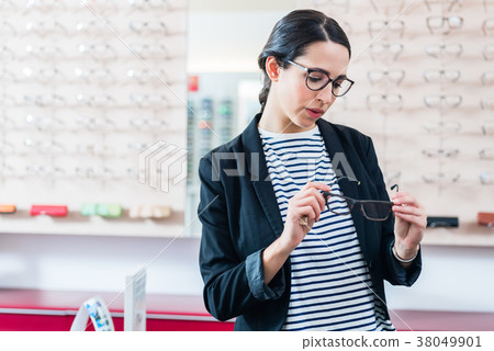 Woman taking glasses off shelf in optician shop Woman taking glasses off shelf in optician shop 38049901