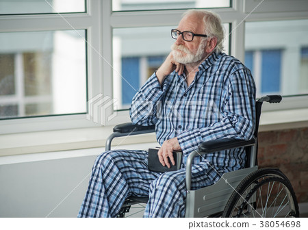 Sad senior male sitting in wheelchair in room Sad senior male sitting in wheelchair in room 38054698