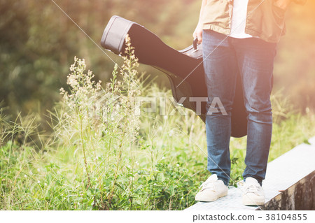 Man dressed in jeans holding guitar case in nature 38104855