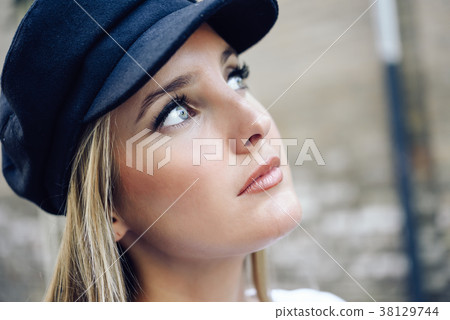 Young blonde woman wearing cap in urban background. Young blonde woman wearing cap in urban background. 38129744