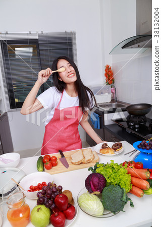 Cheerful woman is covering her eye with spoon in kitchen room 38132004