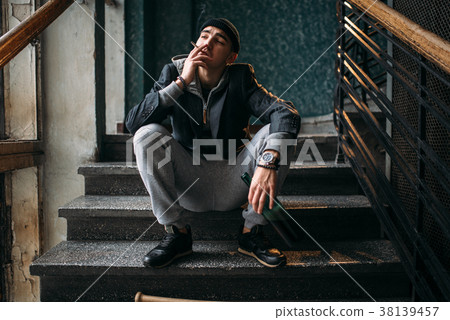 Guy with bottle sits on the stairs and smoking 38139457