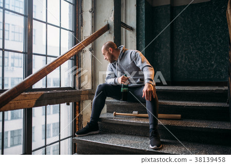 Male theif with baseball bat sits on stairs Male theif with baseball bat sits on stairs 38139458