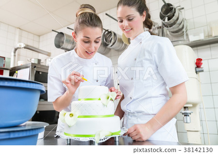 Two pastry bakers decorating large cake 38142130