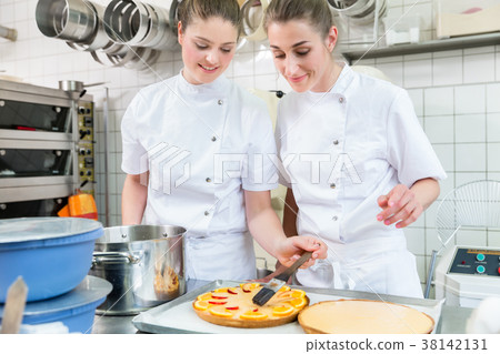 Women putting fruit on cakes in pastry bakery 38142131