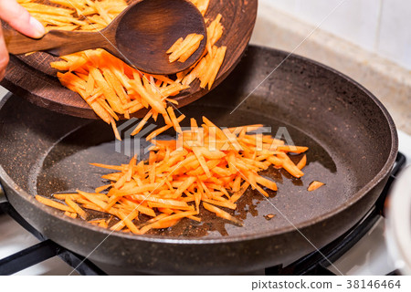 Female hands add chopped carrot to frying pan 38146464
