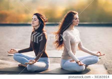 Two young women meditating in Lotus Pose on the roof outdoor 38163914