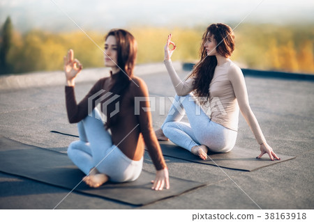 Two young women doing yoga asana half lord of the fishes pose on 38163918