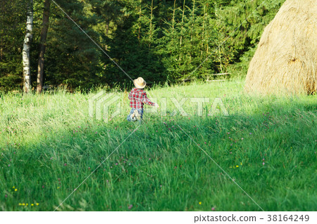 Boy in hat runs grass to forest, view from back 38164249