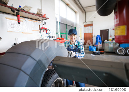 Senior female mechanic repairing a car in a garage Senior female mechanic repairing a car in a garage 38169008