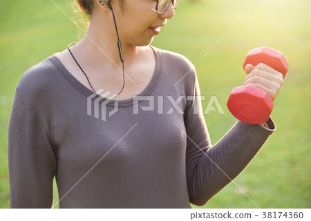 female in grey sportswear is lifting dumbbell. female in grey sportswear is lifting dumbbell. 38174360