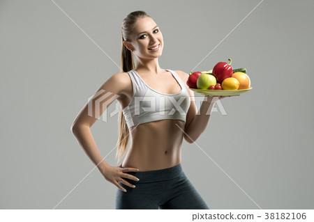 Beautiful young sportswoman holding plate of fruit Beautiful young sportswoman holding plate of fruit 38182106