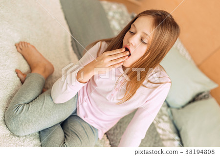 Pleasant teenage girl sitting on bed and yawning 38194808