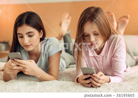 Pretty girls lying on bed and focusing on their Pretty girls lying on bed and focusing on their 38195605