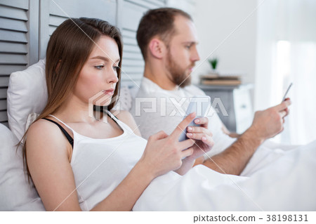 Serious woman and man lying in bed with their 38198131