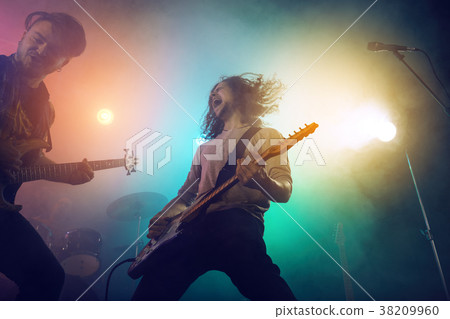 Rock band performs on stage. Guitarist, bass guitar and drums. 38209960