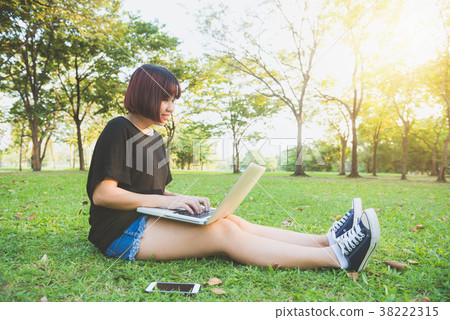 Asian woman working on laptop in park. Asian woman working on laptop in park. 38222315