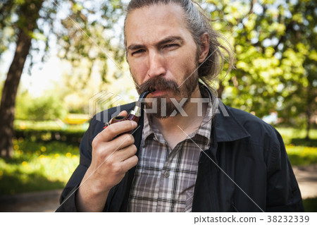 Young serious bearded man smoking pipe 38232339