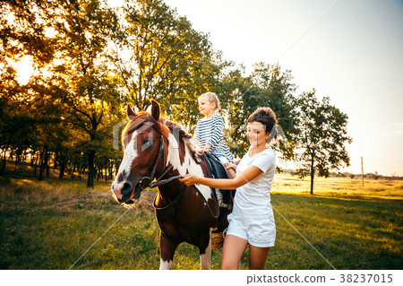 Little girl riding on a horseback with her mother 38237015