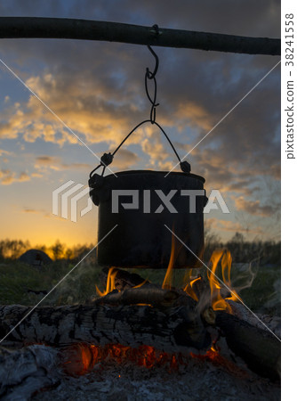 Black pot heating over fire against sunset . Black pot heating over fire against sunset . 38241558
