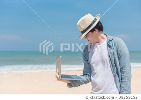 Young Asian man holding laptop on the beach Young Asian man holding laptop on the beach 38255152