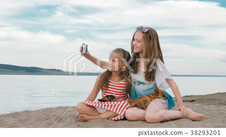Two teenage are sitting on a sandy beach, on the Two teenage are sitting on a sandy beach, on the 38293201