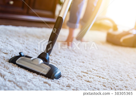 Woman using a vacuum cleaner while cleaning carpet 38305365