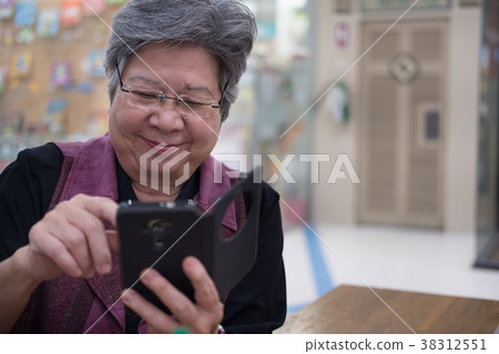 elder woman holding mobile phone in department store. elderly female texting message, using app with smartphone. senior use cellphone to connect with social network elder woman holding mobile phone in department store. elderly female texting message, using app with smartphone. senior use cellphone to connect with social network 38312551