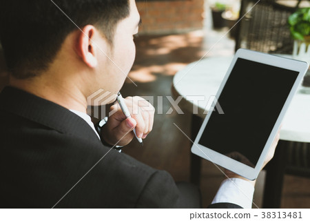 businessman in suit holding touchpad while sitting at cafe. young asian startup man using digital tablet for work at coffee shop businessman in suit holding touchpad while sitting at cafe. young asian startup man using digital tablet for work at coffee shop 38313481
